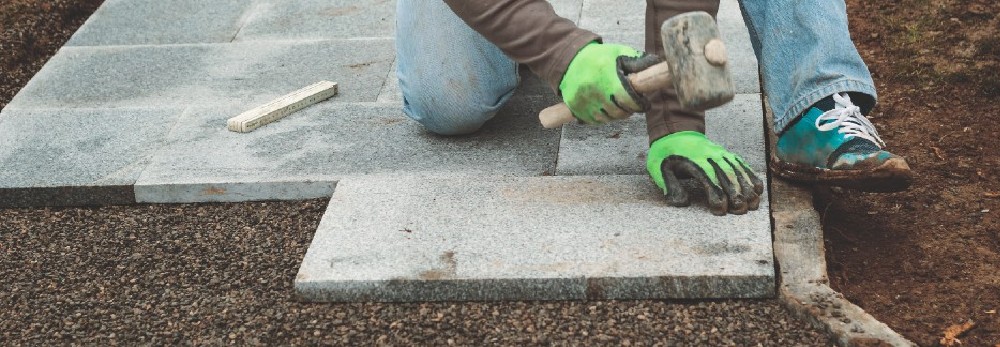 Person verlegt Steinplatten mit Gummihammer